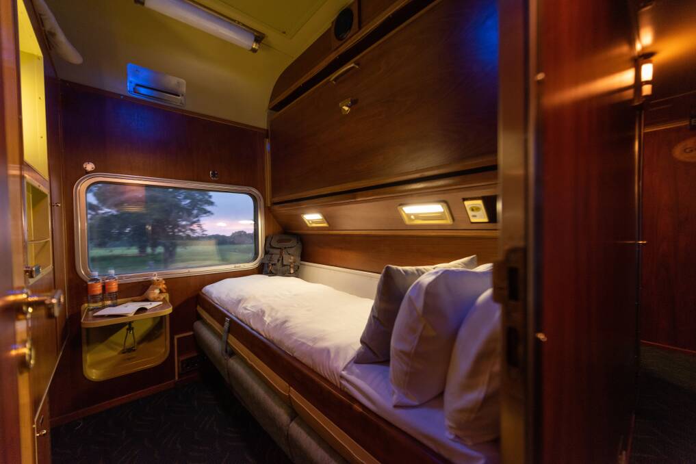 The Gold twin cabin featuring a picture window, three person-wide bench seat turned into a bed, and a drop-down top bunk at night time. Picture: Cam Inniss