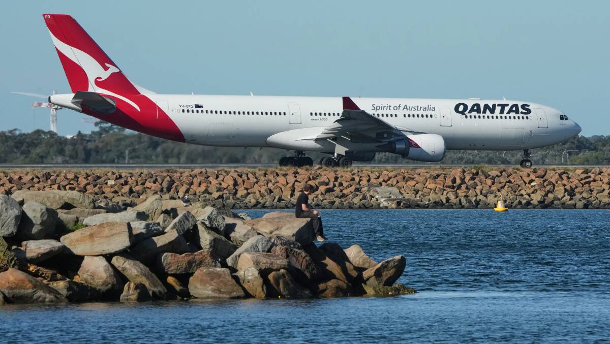 A fisherman sits on the edge of a rock wall on Botany Bay as a Qantas passenger jet prepares for take off from Sydney Airport. Picture by AP/Mark Baker A fisherman sits on the edge of a rock wall on Botany Bay as a Qantas passenger jet prepares for take off from Sydney Airport. Picture by AP/Mark Baker