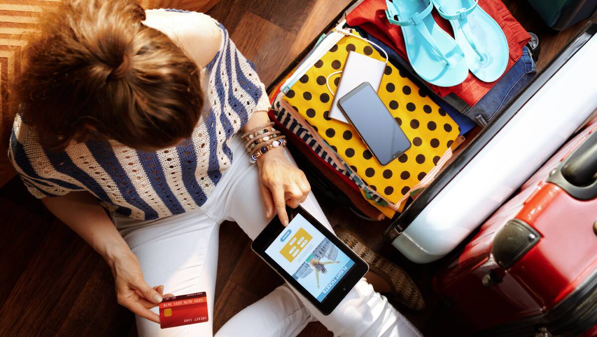 A woman books a flight on her phone with a packed suitcase next to her. Picture by Shutterstock